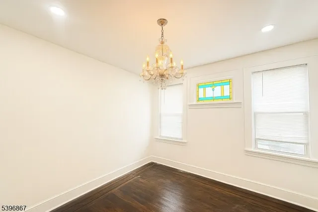 an empty room with wooden floor chandelier and windows