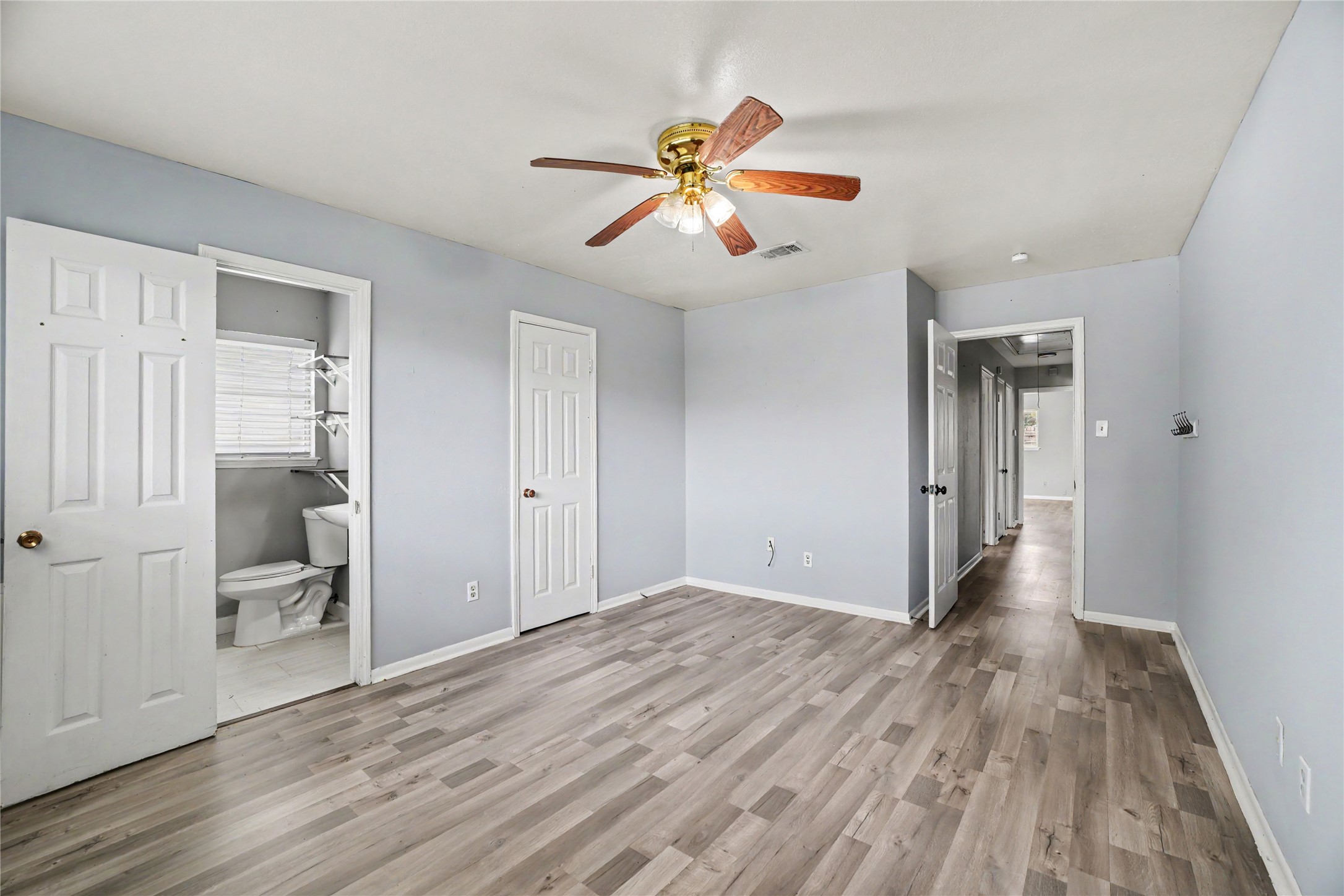 8330 Springtime Lane Houston, TX 77075 - Photo 11 of 27 Primary bedroom with sleek laminate flooring, soft gray walls, a ceiling fan, and an ensuite bathroom for added convenience.