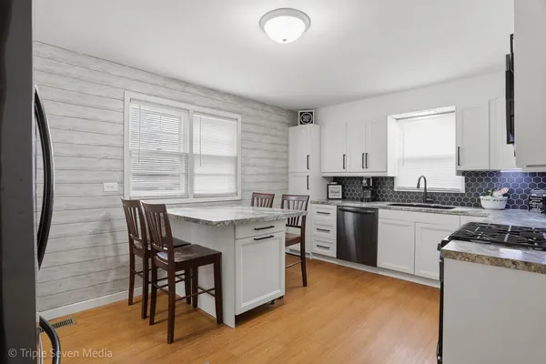 a kitchen with granite countertop a stove top oven a sink dishwasher and white cabinets with wooden floor