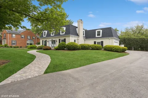 a view of a white house next to a yard with big trees
