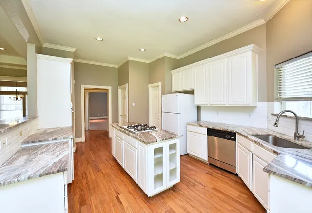 a kitchen with stainless steel appliances a stove a sink dishwasher a refrigerator white cabinets and wooden floor next to a window