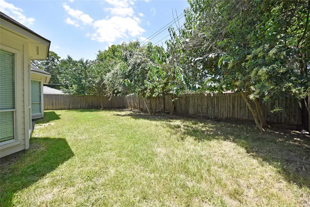 a view of a backyard with large trees and wooden fence
