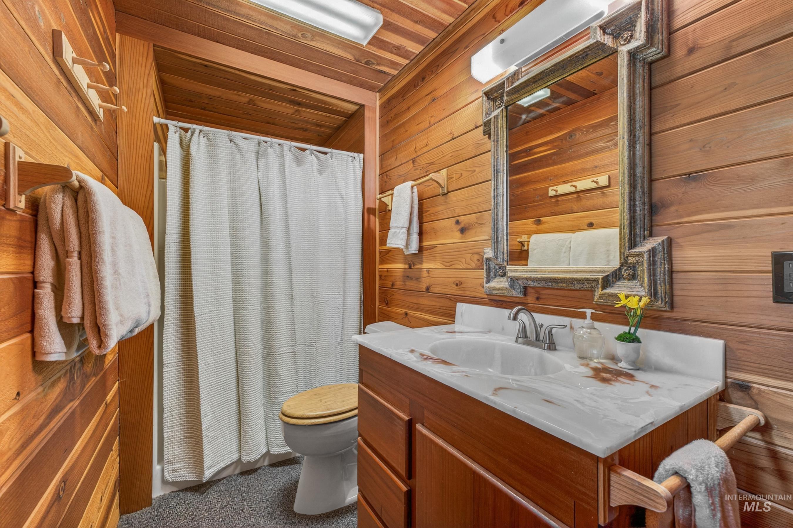 2339 West Mountain Road Donnelly, ID 83615 - Photo 30 of 37 Wood-paneled bathroom featuring a vanity with a white countertop and integrated sink, a framed mirror, and a shower with a white curtain