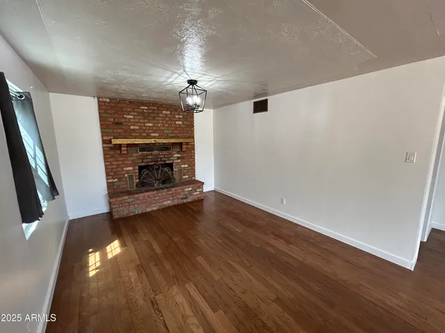 a view of an empty room with wooden floor fireplace and a window