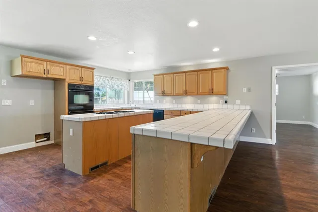 a kitchen with stainless steel appliances granite countertop a stove top oven a sink dishwasher and a refrigerator with wooden floor