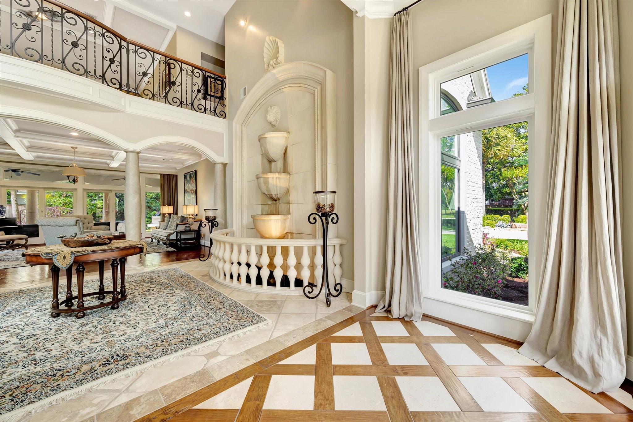 14214 Golf View Trail Houston, TX 77059 - Photo 22 of 49 This elegant living space features a grand, open-concept design with high ceilings, a beautiful indoor fountain, and large windows offering abundant natural light. The room includes sophisticated architectural details such as ornate railings and columns, with a view of lush greenery outside.