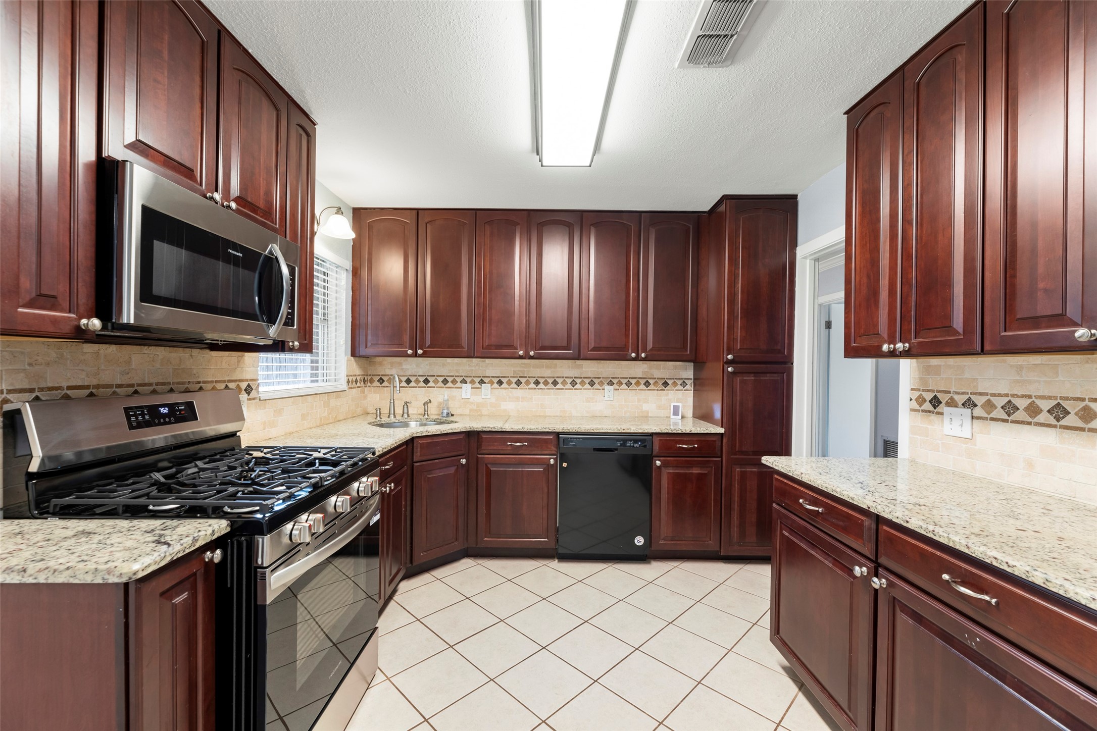 6148 Indigo Street Houston, TX 77074 - Photo 26 of 37 a kitchen with stainless steel appliances granite countertop wooden cabinets a stove top oven a sink and dishwasher