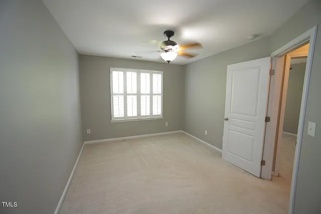 an empty room with chandelier fan and windows