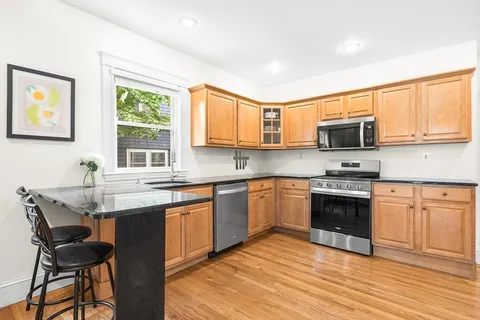 a kitchen with stainless steel appliances granite countertop a stove top oven a sink dishwasher a dining table and chairs with wooden floor