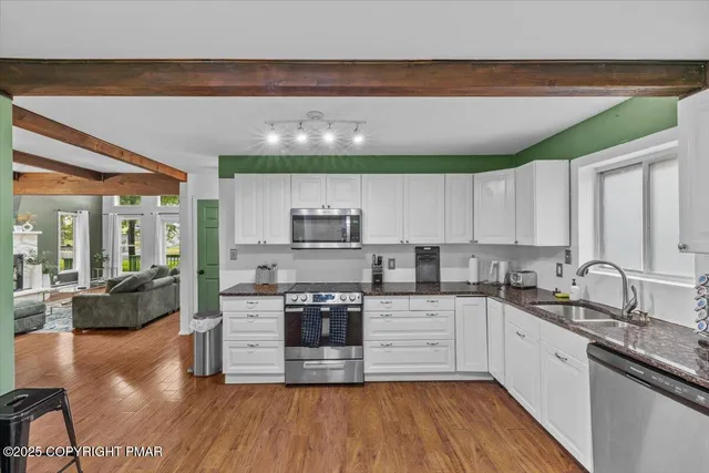 a kitchen with stainless steel appliances a sink dishwasher a stove top oven a refrigerator with white cabinets and wooden floor