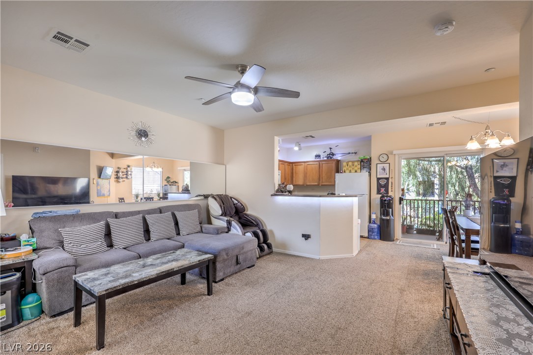 4705 Apulia Drive, Unit 203 North Las Vegas, NV 89084 - Photo 7 of 39 An inviting open-concept living area boasts a ceiling fan, plush carpeting, and seamless access to a balcony for outdoor enjoyment.