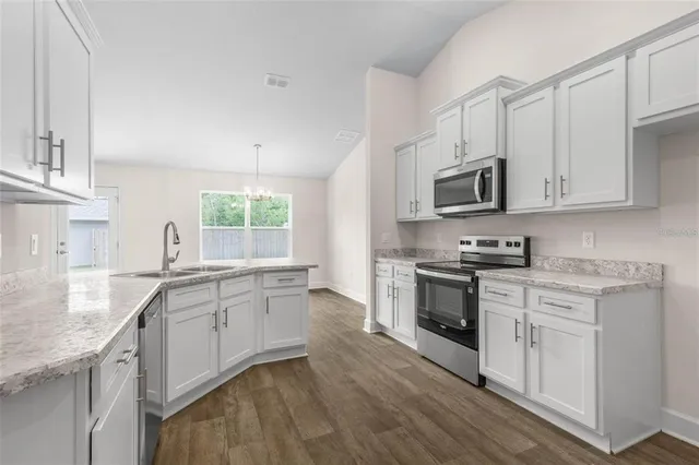 a kitchen with stainless steel appliances granite countertop white cabinets a sink dishwasher a stove and a refrigerator with wooden floor