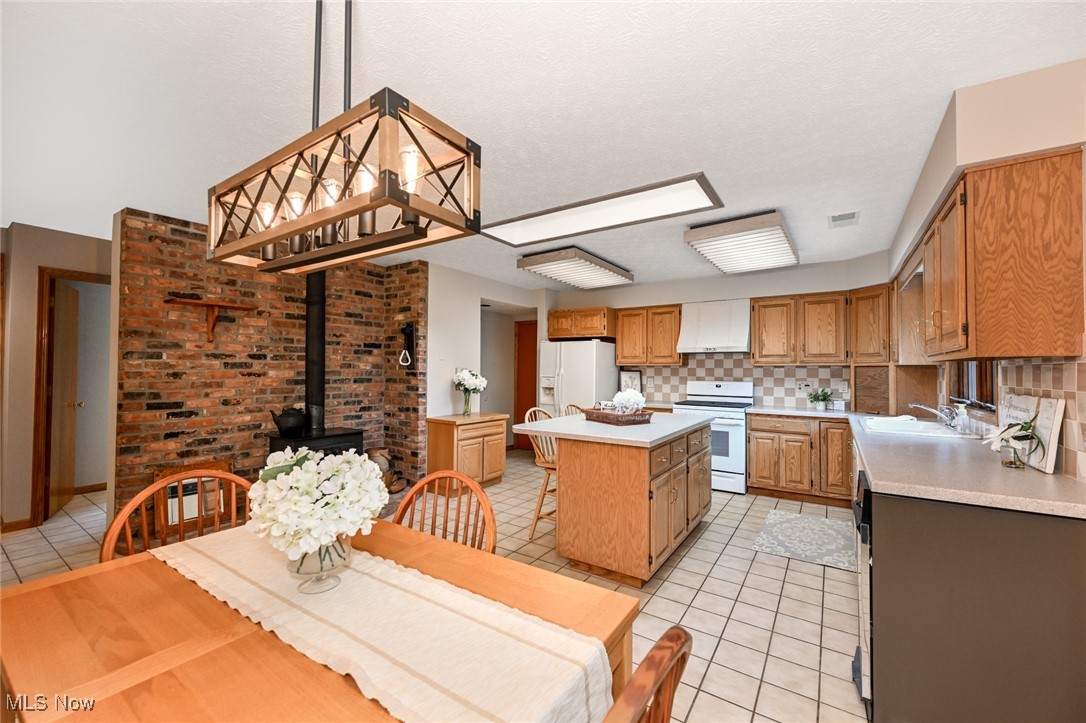 4010 State Road Medina, OH 44256 - Photo 13 of 50 Kitchen with white appliances, light tile patterned floors, light countertops, a kitchen island, and a wood stove
