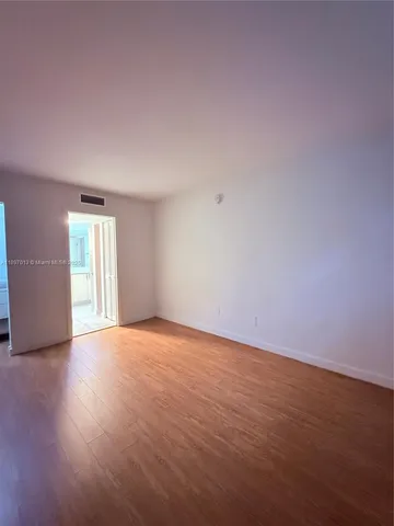 a view of an empty room with wooden floor and window