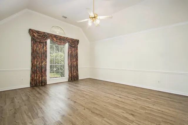 an empty room with wooden floor fan and windows