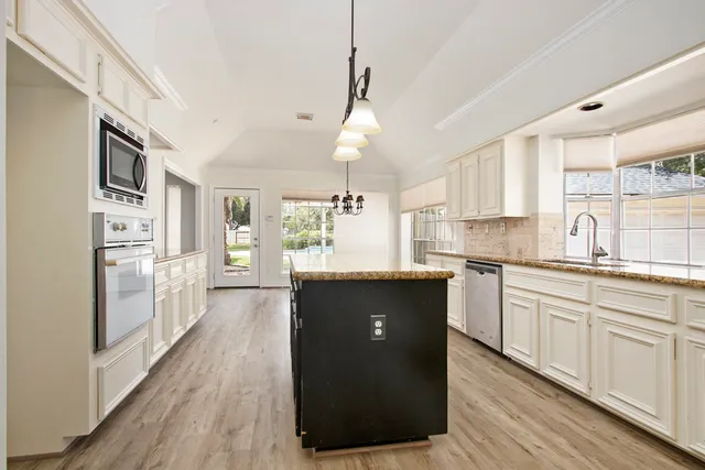 a kitchen with stainless steel appliances granite countertop a refrigerator a sink dishwasher a stove and white countertops with wooden floor