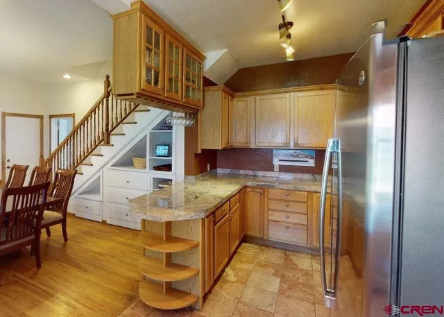 a kitchen with kitchen island granite countertop a refrigerator a stove and a dining table with wooden floor