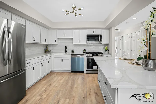 a large kitchen with stainless steel appliances granite countertop a stove a sink dishwasher a refrigerator and white cabinets with wooden floor