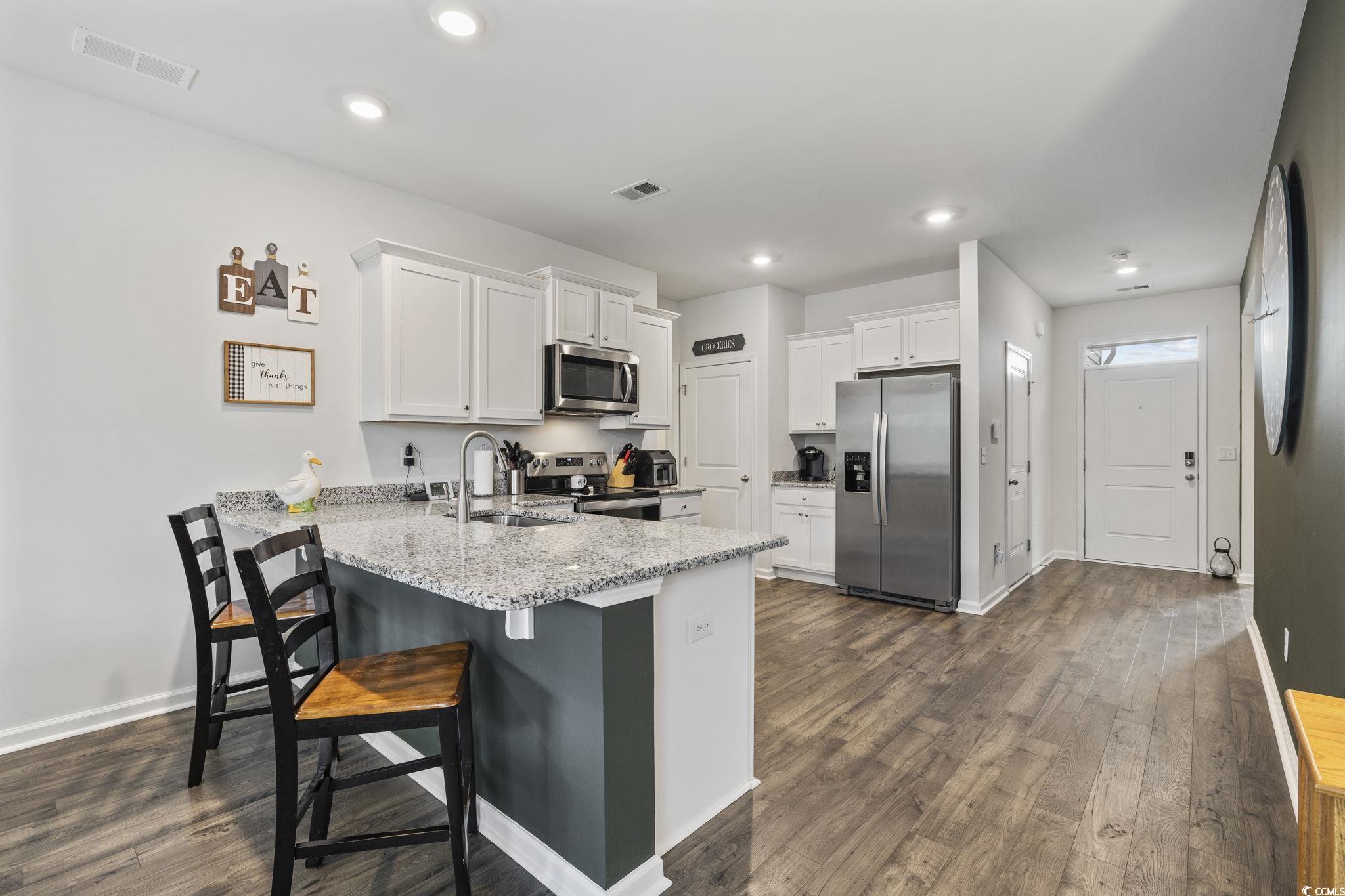 2816 Ophelia Way Myrtle Beach, SC 29577 - Photo 5 of 39 Kitchen with white cabinetry, appliances with stainless steel finishes, a peninsula, a breakfast bar, and light stone counters