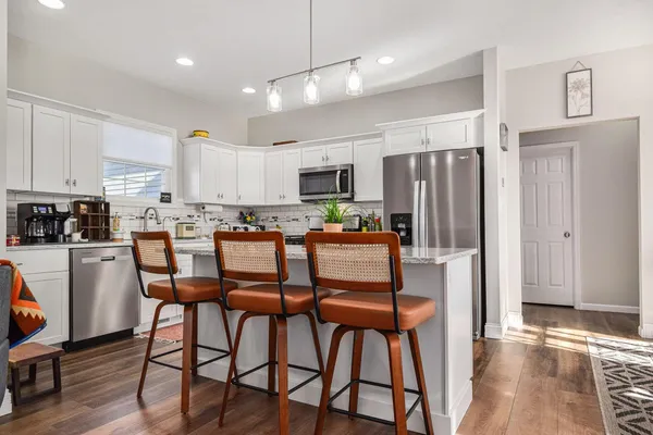 a kitchen with stainless steel appliances a refrigerator a stove top oven a sink dishwasher and white cabinets with wooden floor