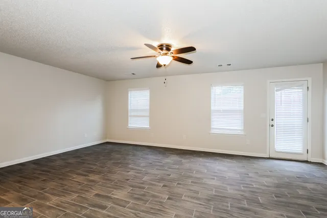 an empty room with chandelier fan and windows