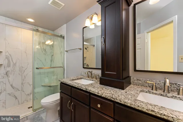 a bathroom with a granite countertop double vanity sink mirror and toilet