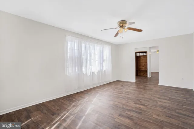 an empty room with wooden floor ceiling fan and windows
