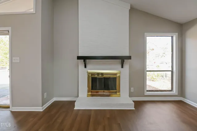 an empty room with wooden floor fireplace and windows