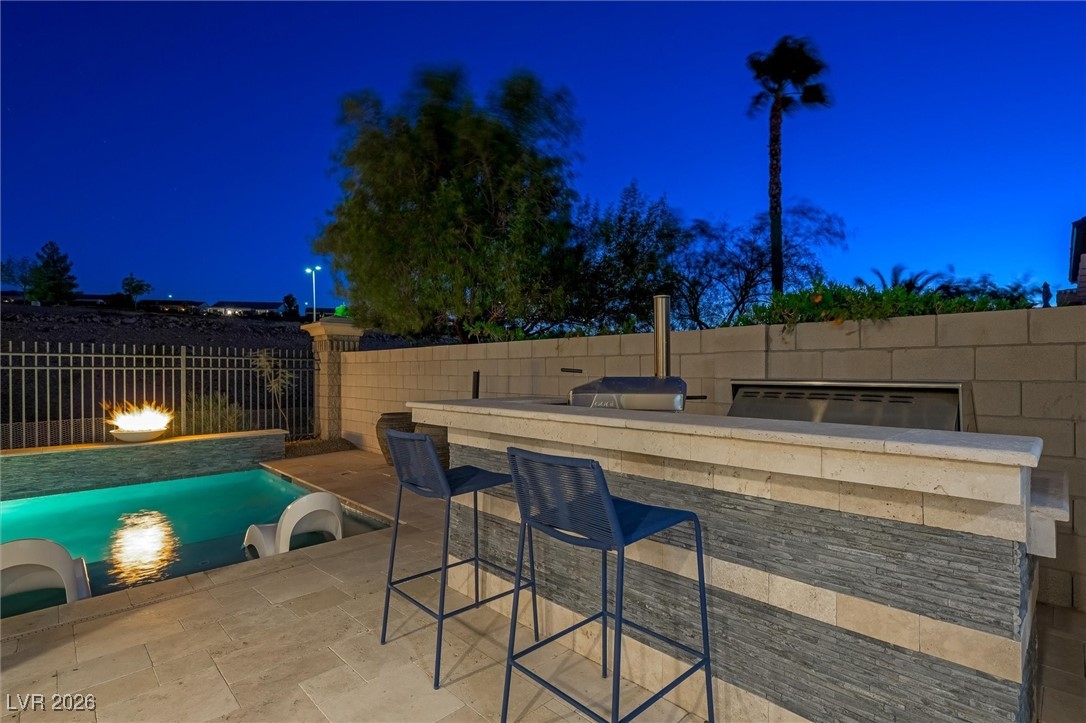 1673 Ravanusa Drive Henderson, NV 89052 - Photo 51 of 66 Pool at night with a fenced backyard, exterior bar, a patio area, and an outdoor kitchen