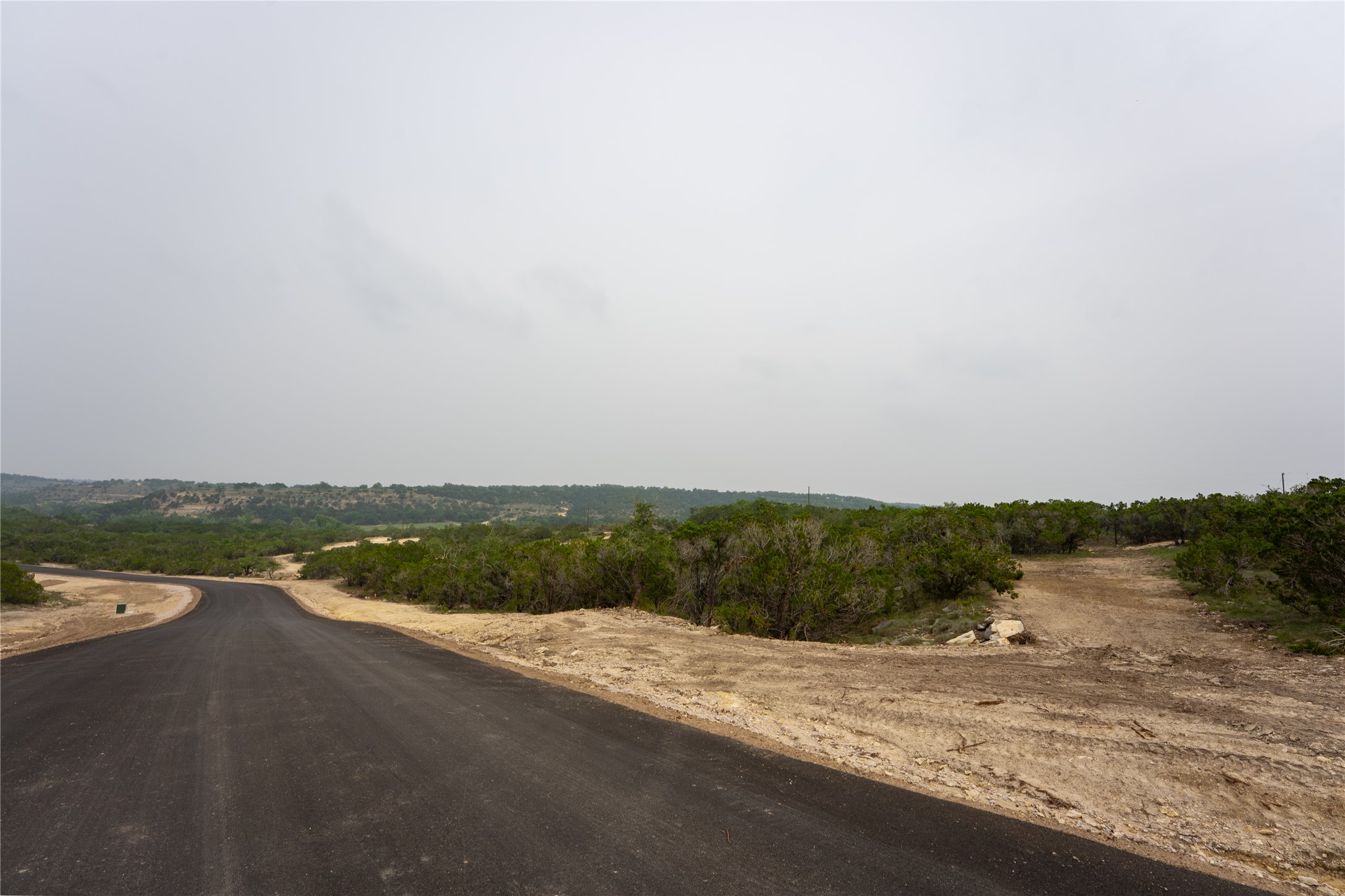 Lot 5 Ranch Road 165 Dripping Springs, TX 78620 - Photo 12 of 12 Paved road curving through a natural landscape with mature vegetation and distant tree lines