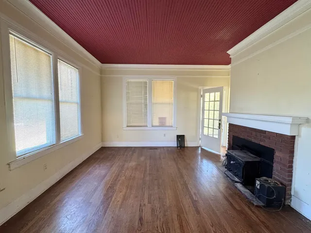 an empty room with wooden floor fireplace and windows