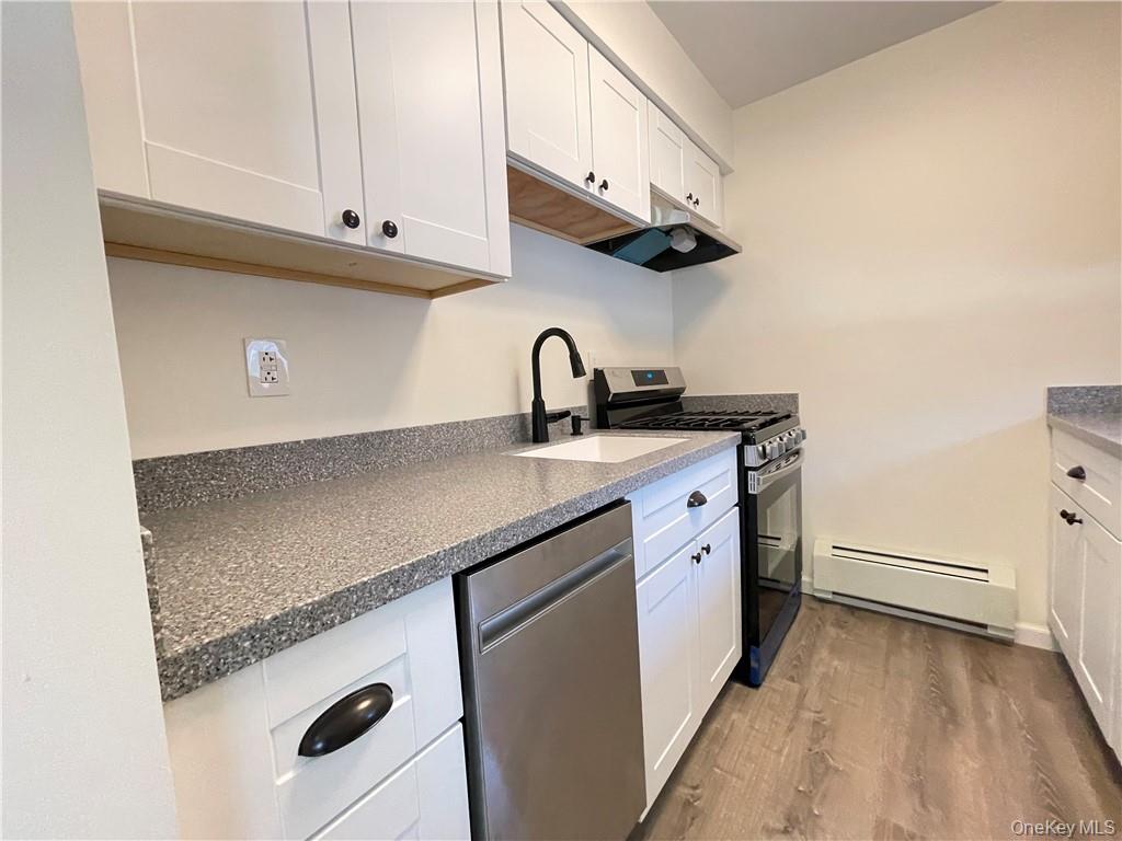 27 Tanager Road, Unit 2702 Monroe, NY 10950 - Photo 6 of 17 Kitchen featuring white shaker cabinetry, speckled countertops, a stainless steel dishwasher, a gas range with an overhead vent, and wood-finish flooring
