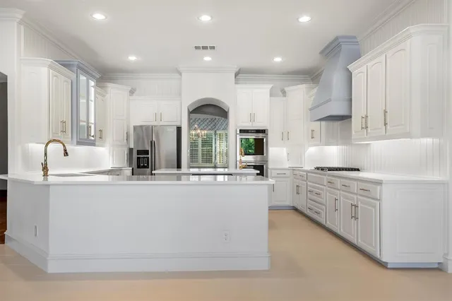 a large kitchen with stainless steel appliances granite countertop a stove a sink a refrigerator and white cabinets with wooden floor