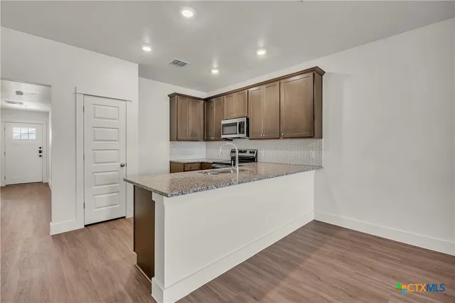 an empty room with wooden floor kitchen view and a refrigerator