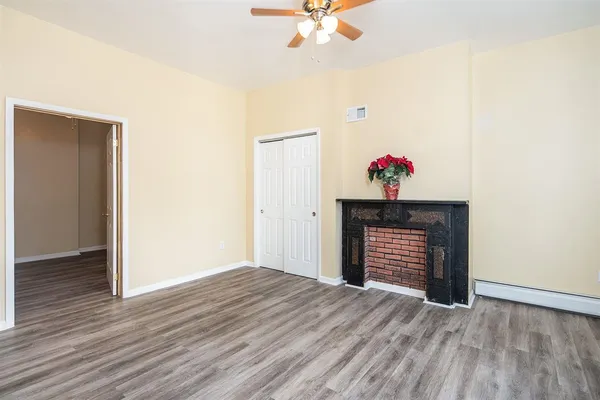 a view of an empty room with wooden floor and fan