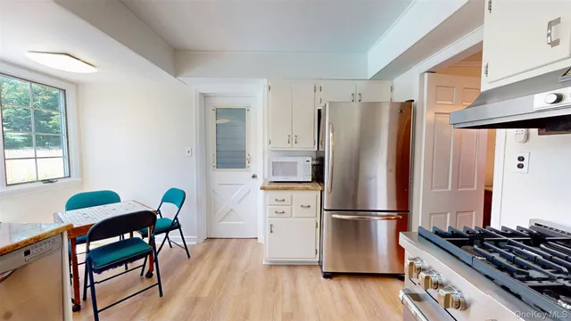 a kitchen with stainless steel appliances a refrigerator a stove a dining table and chairs with wooden floor