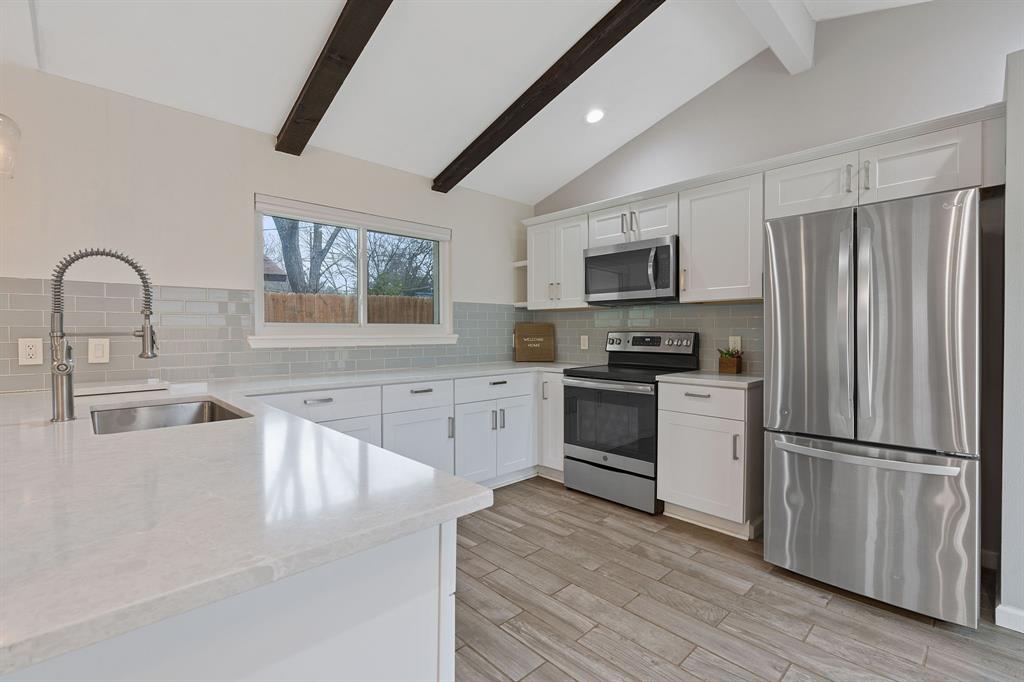 5211 Halmark Drive Austin, TX 78723 - Photo 6 of 27 A well-appointed kitchen features sleek stainless steel appliances, pristine white cabinetry, and charming exposed wooden beams across the ceiling.