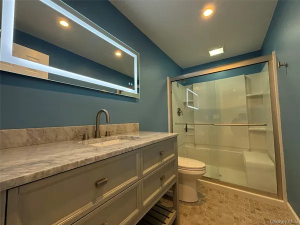 a bathroom with a granite countertop sink a toilet a mirror and shower