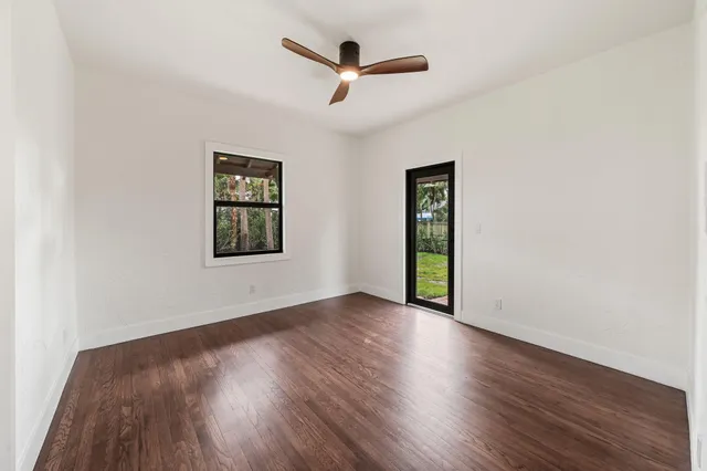 an empty room with wooden floor ceiling fan and windows