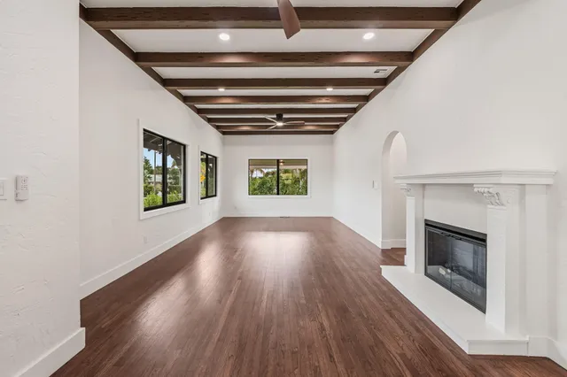 a view of an empty room with wooden floor a fireplace and a window