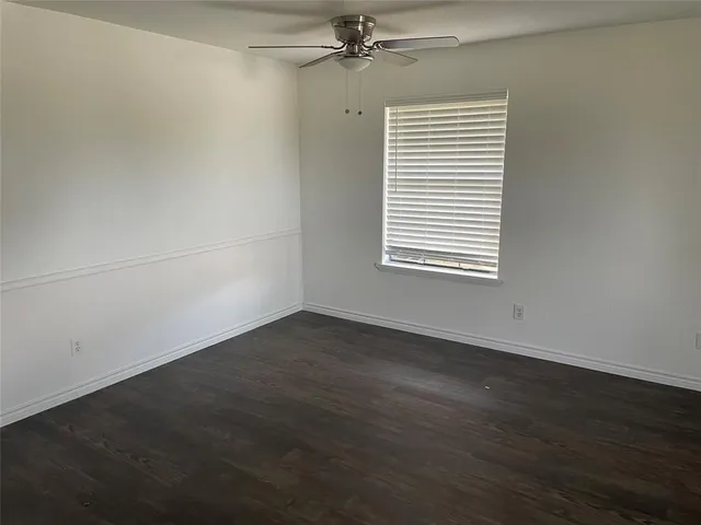 an empty room with wooden floor windows and fan