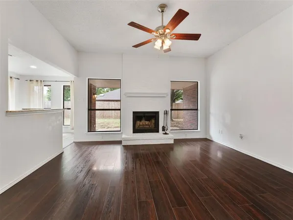 an empty room with wooden floor a ceiling fan and windows