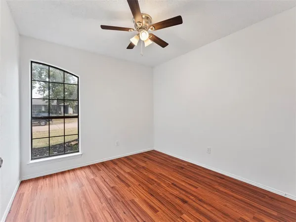 an empty room with wooden floor chandelier fan and windows