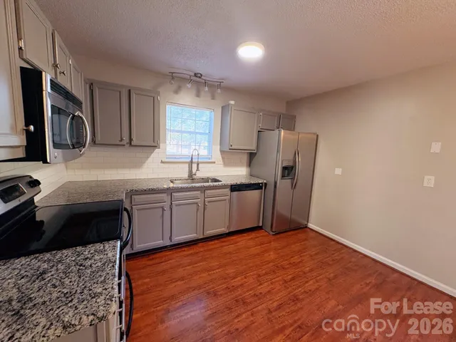 a kitchen with stainless steel appliances granite countertop a sink a stove a refrigerator with grey cabinets and wooden floor