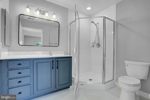a bathroom with a toilet a sink a glass door a shower a mirror a vanity and window