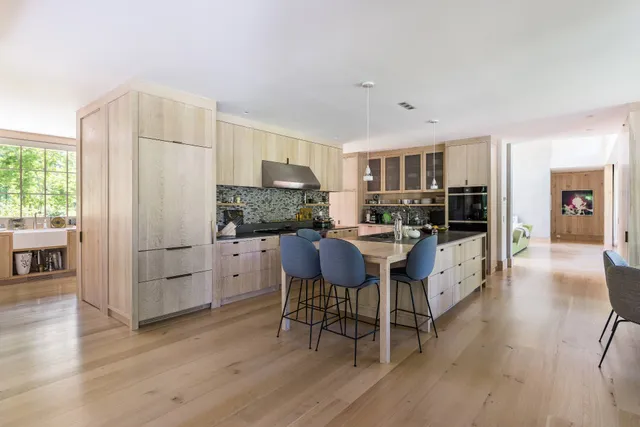 a kitchen with stainless steel appliances kitchen island granite countertop a refrigerator a stove a dining table and chairs with wooden floor