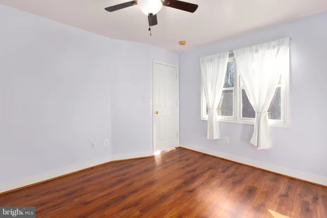 an empty room with wooden floor chandelier fan and windows