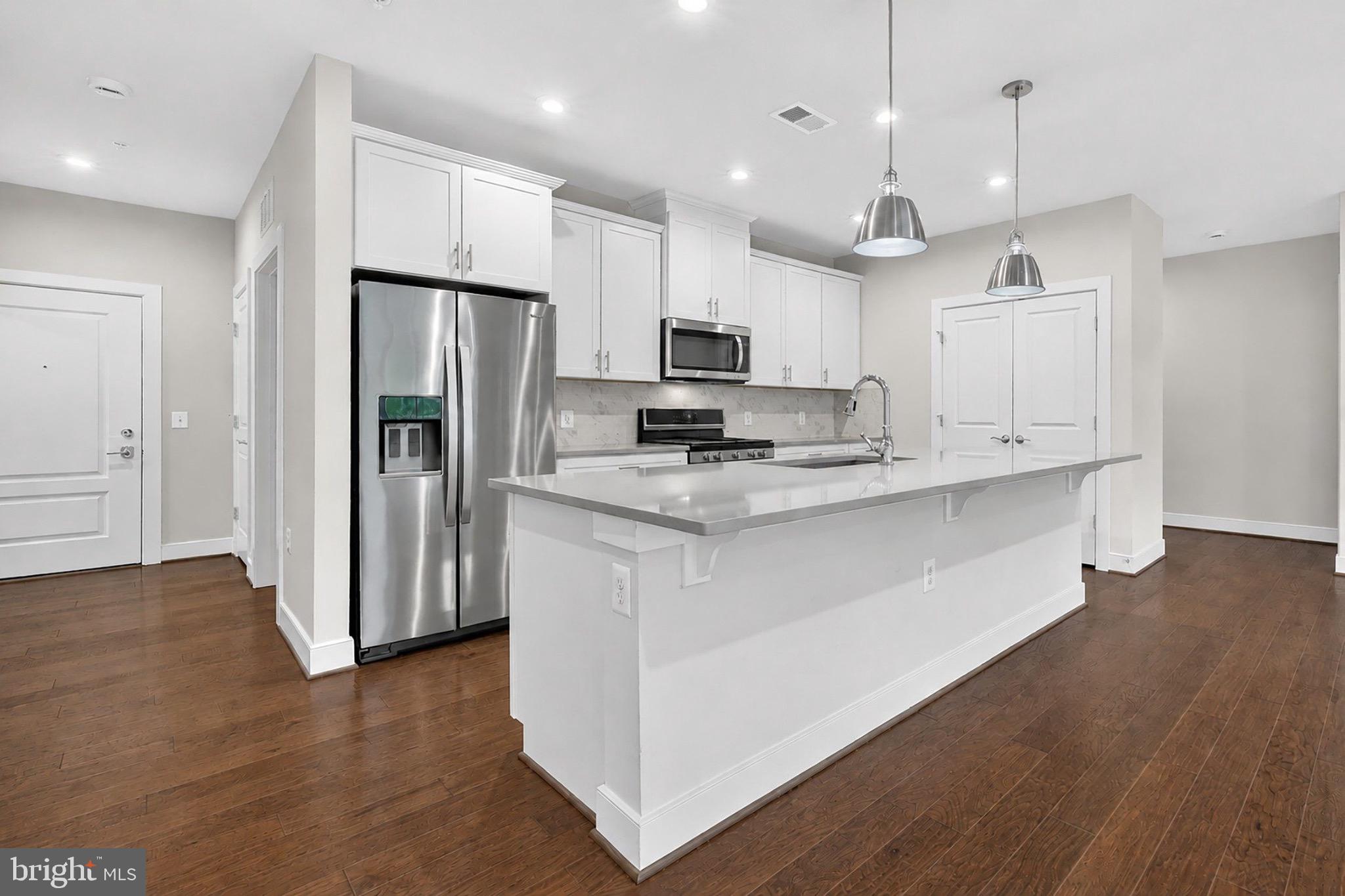 2319 Field Point Road, Unit 102 Herndon, VA 20171 - Photo 7 of 20 a kitchen with kitchen island granite countertop a refrigerator a sink dishwasher a stove and white cabinets with wooden floor