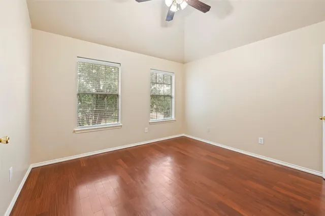 an empty room with wooden floor chandelier fan and windows