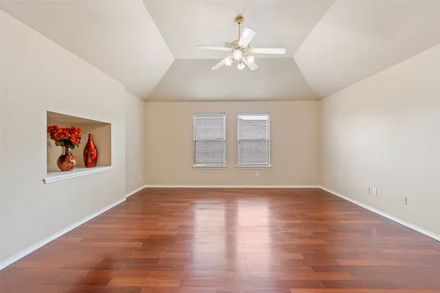 an empty room with wooden floor chandelier fan and windows